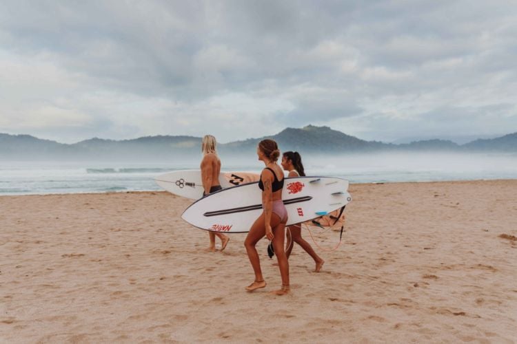 Personen mit Surfboard am Strand beim Surfcamp in Red Island, Bali mit AIFS