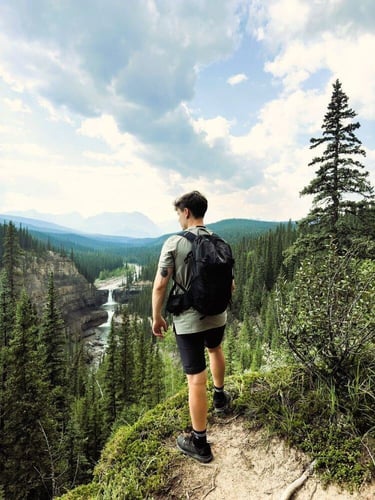 Ein Mann während seines Auslandsjahres mit AIFS auf einem Berg in Kanada. Im Hintergrund ein grüner Wald und ein Wasserfall.