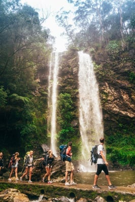 AIFS Australien: Reisegruppe erkundet das Abenteuer mit Rucksäcken am Wasserfall – Entdecke unvergessliche Momente mit AIFS Adventure Trips.