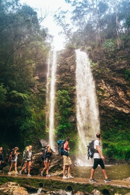 AIFS Australien: Reisegruppe erkundet das Abenteuer mit Rucksäcken am Wasserfall – Entdecke unvergessliche Momente mit AIFS Adventure Trips.