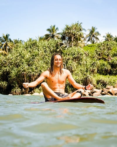 Person meditiert auf einem Surfbrett im ruhigen Wasser vor dem Kabalana Beach in Sri Lanka.