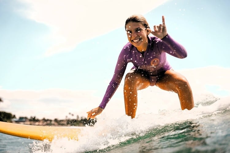 Surferin reitet eine Welle im Surfcamp in Sri Lanka mit strahlendem Sonnenschein im Hintergrund.